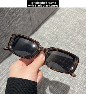 Detail of tortoiseshell rectangle sunglasses featuring grey lenses held in hand