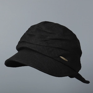 Detail of black cotton linen newsboy cap with gold logo plate and pleated fabric texture