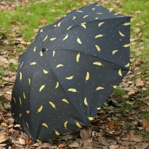 Dettaglio dell'ombrello pieghevole nero con stampa piuma dorata su foglie autunnali