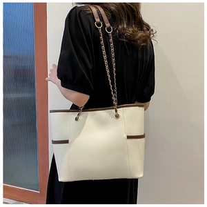 Model wearing a large beige tote bag with chain strap and brown trim side view