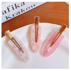 Detailed view of pink marble resin hair clips with golden metal base on a white tray