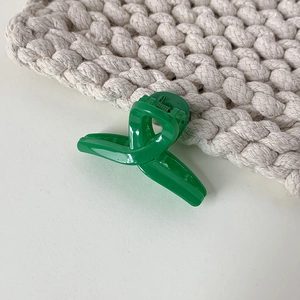 Detailed view of a bright green cross-twist mini hair claw clip on a soft knit fabric