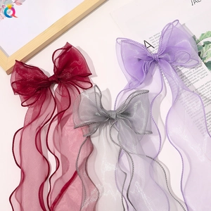 Close-up of three organza bow hair clips with long wavy ribbons in burgundy, grey, and lilac