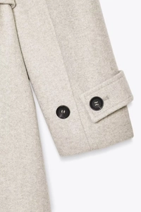 Detailed close-up of light grey wool coat sleeve with buttoned cuff and COS branding
