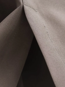 Close-up of taupe woven fabric showing precise stitching and fine texture of the garment
