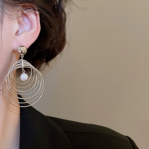 Detail of multi-layer silver circular earrings with a white pearl pendant on model