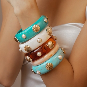 Détail de bracelets joncs en résine superposés avec perles et coquillages dorés