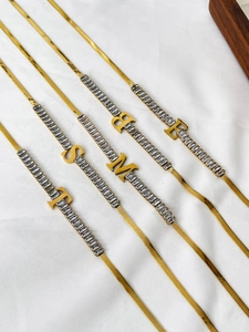 Detailed view of 18K gold flat snake chains with zircon inlay and alphabet letter pendants