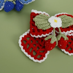 Handmade crochet hair clip with red strawberry bow and green leaves on soft background