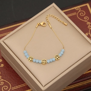 Bracelet chaîne dorée élégant avec perles bleues mates et breloques Arbre de Vie sur coffret