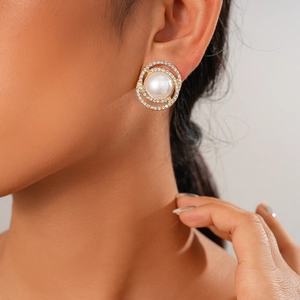 Close-up of a gold round stud earring with large pearl and sparkling zircon halo