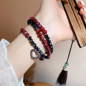 Detail of layered beaded bracelet with rhodochrosite stones and silver heart charm