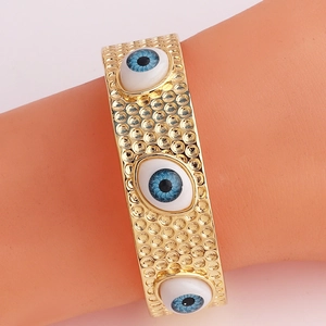 Détail d'un bracelet jonc doré avec trois yeux maléfiques bleus et blancs sur un modèle