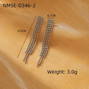 Detalle de aretes de borla larga plateada de 6,5x0,7 cm sobre tela de satén amarillo