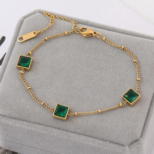 Elegant gold titanium steel bracelet with square emerald green gemstones on velvet tray
