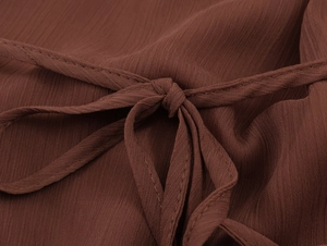 Detailed macro view of dark brown woven chiffon fabric and adjustable waist tie knots
