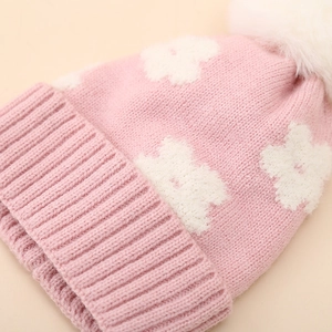 Close-up of pink winter knit baby hat with white flower patterns and fluffy pom pom