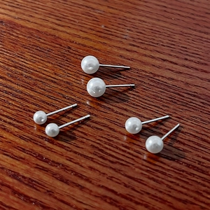 Three-pair silver needle pearl stud earring set in varied sizes on wooden surface