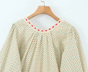 Detail van beige bloementop met fruitmotief, kanten rand en rood decoratief lint