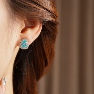 Detail view of blue zircon gourd earrings with silver settings on a female model