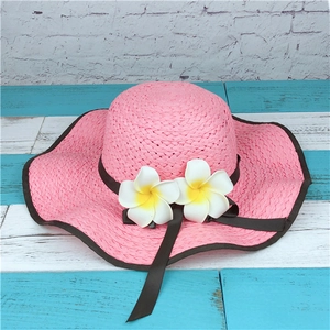 Detailed view of pink straw sun hat featuring plumeria flowers and ribbon on wavy wide brim