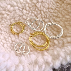 Detail of twisted hoop earrings in gold and silver S925 on a soft white texture