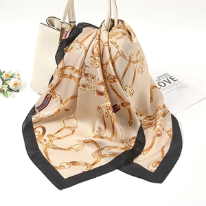 Detail of champagne gold and black silk scarf with chain pattern tied to a white handbag