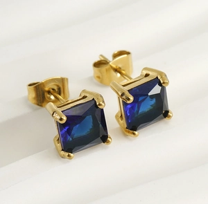 Detail shot of square blue zircon earrings with gold plating on a textured backdrop