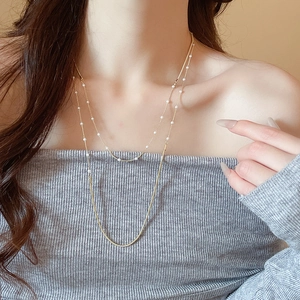 Detail of layered gold snake chain necklace with pearl accents on a model's neck