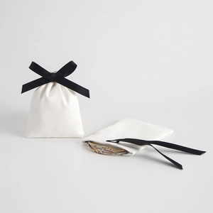 White velvet drawstring jewelry pouch with black ribbon bow featuring a gold bracelet