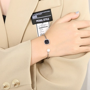 Silver open bangle with square blue gemstone and pearl shown on a model wrist
