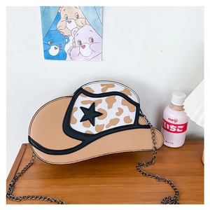 Detail of cowboy hat-shaped crossbody bag with cow print and star motif on wood