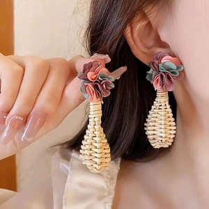 Detail of hand-woven straw flower earrings with soft fabric petals on model