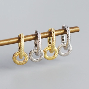 Detailed view of twisted gold and silver hoop earrings with gemstone charms on a metal bar