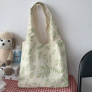 Detail of a minimalist cream canvas tote bag with green leaf print on a checkered cloth