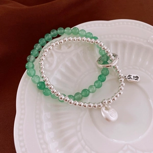Close-up of stacked jade bead bracelet with silver Fu lock pendant on ceramic plate