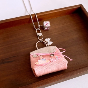 Close-up of pink fabric kitty bag pendant with silver chain and bow detail