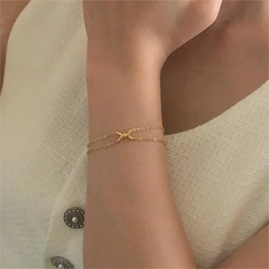 Minimalist double layer gold chain bracelet with X-shaped charm worn on female wrist