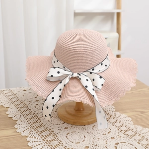 Detail of pink straw sun hat with wavy brim and black and white polka dot ribbon bow