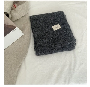 Close-up of soft dark grey wool knit scarf with egg label on a cozy white fabric background