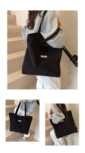 Detail of a large black corduroy tote bag featuring stripe texture and fashion label