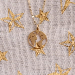 Detail view of gold stainless steel world map necklace on starry fabric background