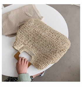 Detail of cream straw woven beach bag with square wooden handle on a white table