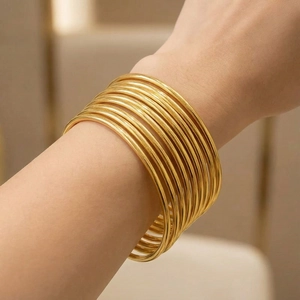 Close-up of model wearing layered 3mm golden stainless steel slim bangle bracelets
