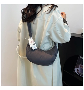 Close-up of a dark grey crescent shoulder bag with a white rabbit plush keychain