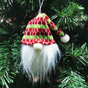 Close-up of knit Christmas gnome pendant with red hat hanging on green tree branches