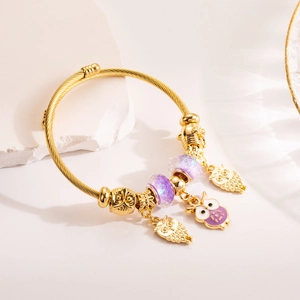 Adjustable golden twisted bangle featuring purple beads and owl charms on white stone