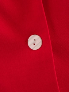 Gros plan sur le tissu rouge et le bouton nacré blanc d'un tailleur pantalon