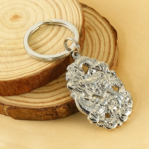 Polished silver stainless steel dragon keychain pendant on a rustic wooden display base