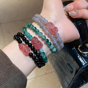 Detail of beaded agate bracelets with red Pi Xiu charm worn on a wrist with a leather bag